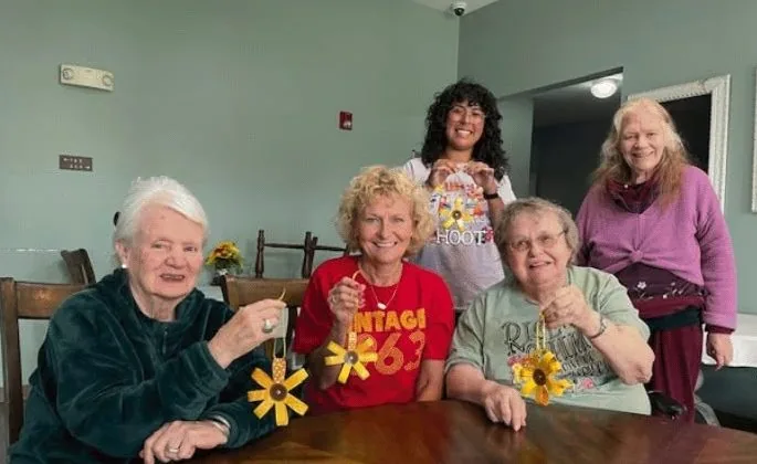 Residents and caregivers smiling together during a craft activity at Century Assisted Living